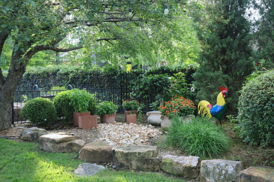 rock garden with potted plants, shrubs, and a colorful metal rooster